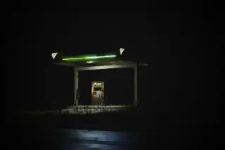 Illustration: A single lit fuel pump station stands in complete darkness at night.