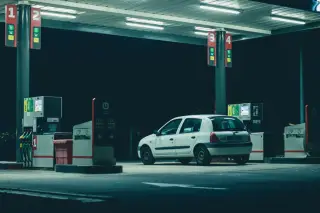Illustration: A white car parked at an illuminated gas station pump at night.