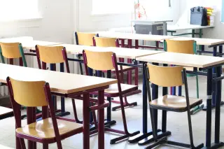 Illustration: Rows of empty desks and chairs in a brightly lit classroom.