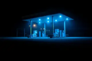 Illustration: An empty gas station forecourt illuminated with blue light at night.