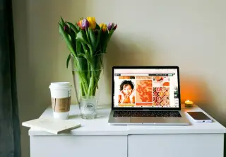 Illustration: A laptop open on a white desk beside a coffee cup, smartphone, and a vase of colourful tulips.