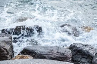 Illustration: Ocean waves churning and splashing against dark coastal rocks.