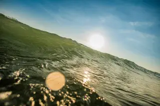 Illustration: Close-up of a rising ocean wave with the sun shining in a blue sky.