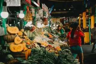 Illustration: A bustling indoor market stall packed with fresh vegetables and produce under hanging lights.