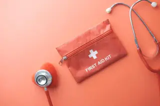 Illustration: A first aid kit pouch, stethoscope, and small red heart model lying on a salmon-pink surface.