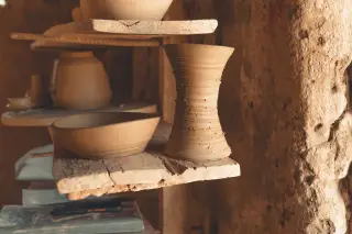 Illustration: Unfinished clay pottery rests on rustic wooden shelves in an artisan workshop.