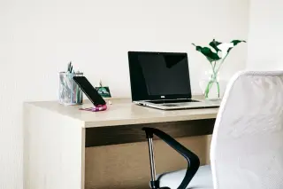 Illustration: A bright modern workspace with a laptop, smartphone stand, and an office chair by a wooden desk.