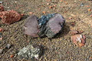 Illustration: Close-up of a cut volcanic rock lying on coarse volcanic soil and gravel.