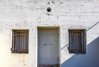 Illustration: A sturdy steel door and barred windows on a weathered concrete building.