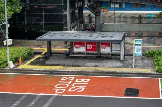 Illustration: A modern roadside bus stop shelter with red bus lane markings on the street.