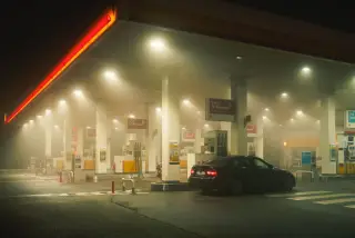 Illustration: A car parked at an illuminated, misty gas station at night.