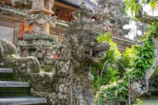Illustration: An ornate stone dragon statue at the entrance stairs of a traditional Balinese temple.