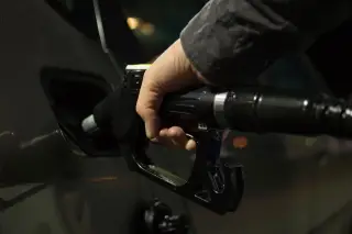 Illustration: A close-up shot of a hand holding a fuel pump nozzle inserted into a vehicle.