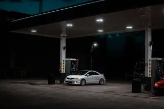 Illustration: A white car parked at an illuminated petrol station at night.