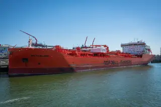 Illustration: A large red oil tanker ship docked at an industrial port under a clear blue sky.
