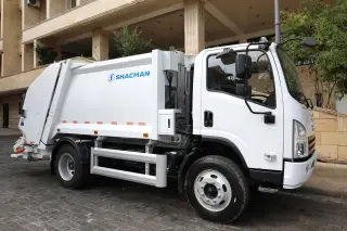 Illustration: A clean white garbage truck parked on a paved street beside a building.