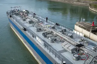 Illustration: An industrial inland tanker barge with pipes and pumps navigated through a canal lock.