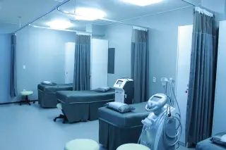 Illustration: An empty clinic or medical room with beds separated by curtains and medical equipment.