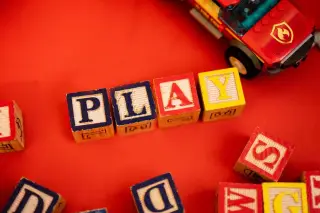 Illustration: Wooden alphabet blocks spelling the word PLAY alongside a toy vehicle on a red surface.