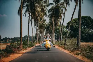 Illustration: A couple rides a yellow scooter down a tropical road lined with tall palm trees.