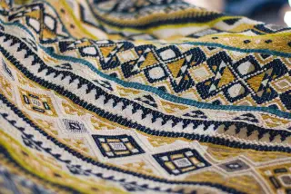 Illustration: Close-up of a woven textile fabric with detailed geometric patterns in blue, yellow, and white.