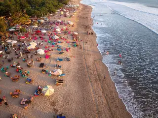 Illustration: Aerial view of a crowded sandy beach with colourful umbrellas and people by the sea.
