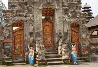 Illustration: A stone Balinese temple gate decorated with ornate golden carved wooden doors and statues.