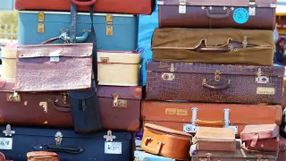 Illustration: A colorful stack of various vintage suitcases and briefcases piled outdoors.