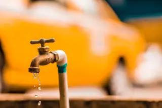Illustration: Close-up of a brass tap dripping water against a blurred yellow background.