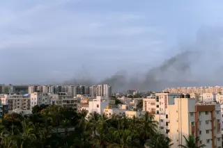 Illustration: Dark smoke drifts in the sky above urban apartment buildings and palm trees.
