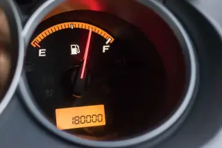Illustration: A close-up of an illuminated car fuel gauge showing a full tank and digital odometer.
