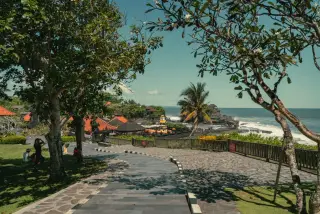 Illustration: A stone pathway overlooking coastal scenery with trees and ocean under a sunny sky in Bali.