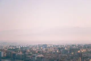 Illustration: A wide view of a city covered in dense atmospheric haze with distant mountains.