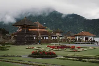 Illustration: Traditional Balinese temple structures with landscaped flowerbeds in front of misty forested hills.