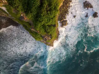 Illustration: Aerial view of steep green cliffs meeting breaking ocean waves with tiny figures standing on the edge.