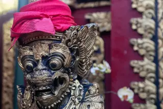 Illustration: Close-up of a carved Balinese statue adorned with a bright pink headcloth.