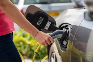 Illustration: A close-up of a person plugging a charging cable into an electric car outdoors.