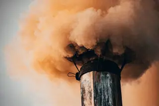 Illustration: Thick orange-brown smoke billows from a weathered metal smokestack into the air.