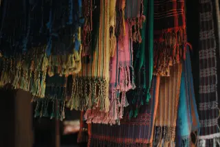 Illustration: Close-up of colorful woven traditional textiles with tassels hanging in a display.