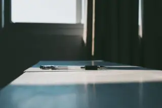 Illustration: A single pen lying on a desk in front of a window with soft light.