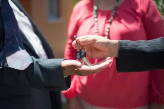 Illustration: Close-up of a person in a suit handing over house keys to another person.