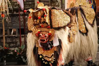 Illustration: An ornate Balinese Barong Ket costume with golden headdress and fur body during a traditional performance.