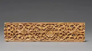 Illustration: An ornate carved ivory or bone cover of a palm-leaf manuscript against a neutral grey background.