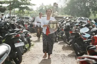 Illustration: A Balinese woman carrying an offering box walks through a crowded motorcycle parking area.