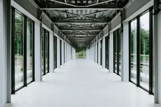 Illustration: A long, bright, empty modern hallway with glass windows and a metal beam ceiling.