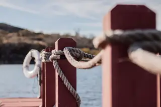Illustration: Thick rope tied along wooden posts on a dock with a lifebuoy visible in the background.