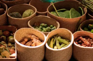 Illustration: Various fresh vegetables and root crops displayed in woven baskets at a market.