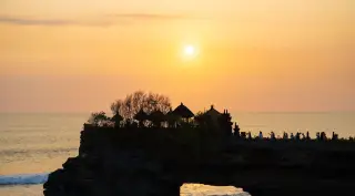 Illustration: Silhouette of Tanah Lot temple on a rocky outcrop against a sunset sky.