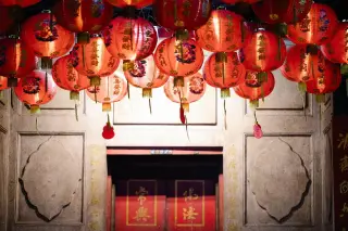 Illustration: Red Chinese lanterns hanging in front of a stone building with traditional inscriptions.