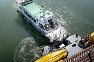 Illustration: A passenger ferry boat docking at a pier with a crew member securing a rope.